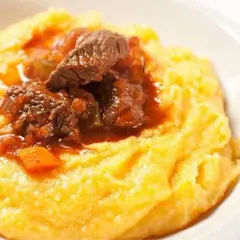 Un invitante spezzatino con piselli, servito su un letto di morbida polenta gialla. Un piatto confortante e saporito.