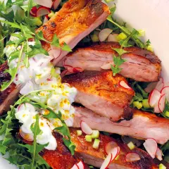 Costine di maiale succulente, perfette per una marinatura saporita, servite su un letto di rucola e ravanelli, con una salsa cremosa.