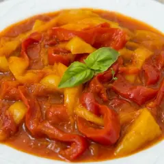 Peperonata ricetta della nonna: peperoni rossi e gialli cotti lentamente in un sugo saporito, guarniti con una fogliolina di basilico fresco.