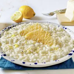 Un cremoso riso al limone freddo, guarnito con scorza di limone e parmigiano grattugiato, pronto per essere gustato.