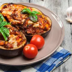 Melanzane alla siciliana, gustoso piatto con melanzane ripiene, pomodorini e basilico fresco, su un tavolo di legno.