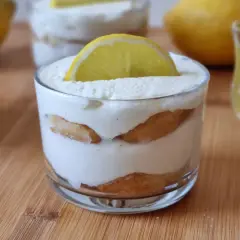 Delizioso tiramisù al limoncello in bicchieri, guarnito con una fetta di limone. Accanto, un bicchierino di limoncello e savoiardi.