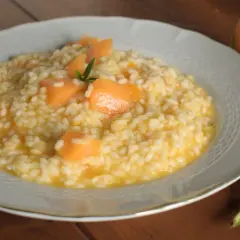 Un cremoso risotto con pezzi di melone e un rametto di rosmarino, accanto a una fetta di melone.
