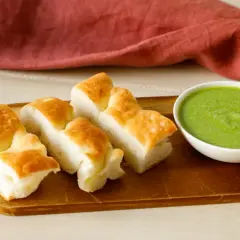 Focaccia tagliata a pezzi su tagliere di legno, accanto una ciotolina con pesto di salvia.