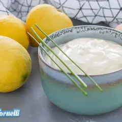 Una ciotola di cremosa maionese allo yogurt, guarnita con erba cipollina, accanto a limoni freschi e uova.
