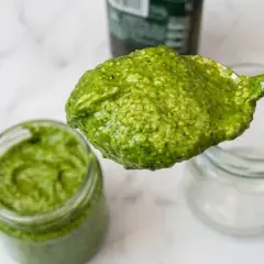 Un cucchiaio pieno di pesto fatto in casa, verde brillante, pronto per essere gustato.
