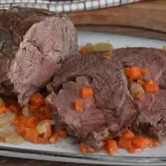 Arrosto di vitello morbido con sughetto e verdure. La carne è succulenta e tagliata a fette, immersa in un delizioso sughetto con carote e sedano a cubetti.