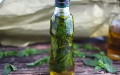 Olio al basilico fatto in casa da Benedetta, profumato e verde brillante, in una bottiglia su un tavolo di legno.