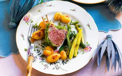 Carrè di agnello croccante con patate novelle e zucchine, un piatto elegante su un piatto fiorito.