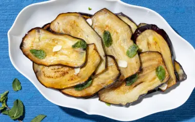 Fette di melanzane grigliate, guarnite con menta fresca e aglio, un contorno di verdure saporito e colorato.