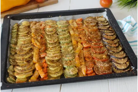 Vassoio con verdure al forno saporite disposte a raggiera: zucchine, carote, peperoni, pomodori e melanzane, condite con pangrattato.