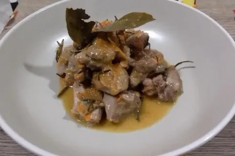 Delizioso spezzatino di tacchino in umido, con erbe aromatiche e una foglia di alloro, servito in una ciotola bianca.