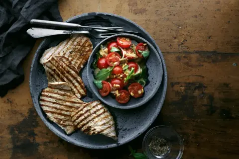 Delizioso paillard di vitello grigliato servito con un'insalata fresca di pomodorini, basilico e pinoli.