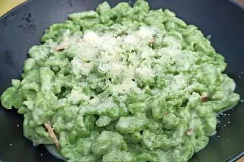Spätzle alla tirolese verdi, conditi con panna e parmigiano, serviti in un piatto nero.