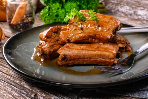 Succulente costine in umido, condite con erbe aromatiche e servite su un piatto scuro. Un piatto invitante e saporito.