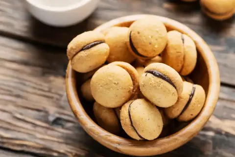 Baci di dama, deliziosi biscotti con ripieno di cioccolato, in una ciotola di legno su un tavolo rustico.