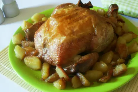 Un succulento pollo allo spiedo dorato, servito su un piatto verde brillante con patate arrosto.