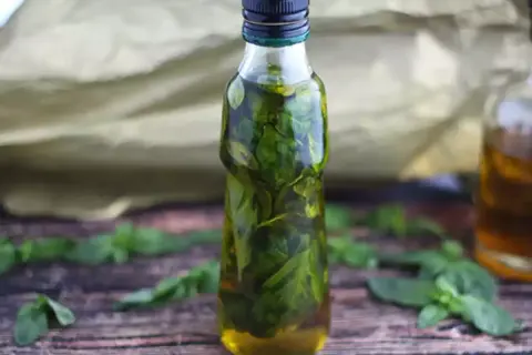 Olio al basilico fatto in casa da Benedetta, profumato e verde brillante, in una bottiglia su un tavolo di legno.