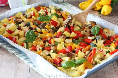 Un colorato mix di verdure in padella, con patate, peperoni, zucchine e melanzane, guarnito con basilico fresco.