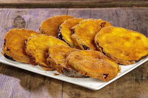 Fette di melanzane fritte solo con farina, dorate e croccanti, servite su un piatto bianco.