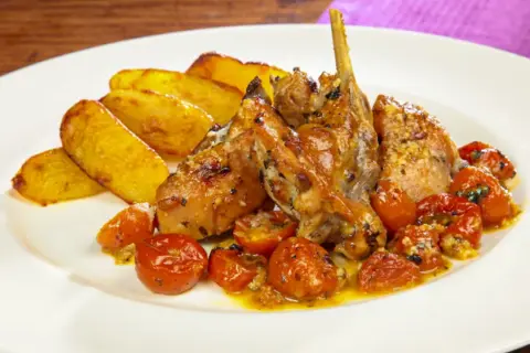 Delizioso coniglio al forno con patate arrosto e pomodorini confit, un piatto succulento e saporito.