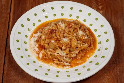 Un piatto di trippa alla fiorentina, ricca e saporita, cosparsa di parmigiano, servita su un piatto bianco decorato.