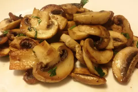 Funghi champignon in padella, dorati e succulenti, guarniti con prezzemolo fresco. Un contorno semplice e gustoso.