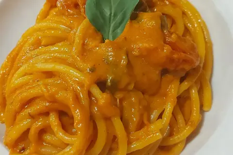 Un piatto invitante di pasta con i pomodorini, condita con una salsa cremosa e guarnita con una foglia di basilico fresco.