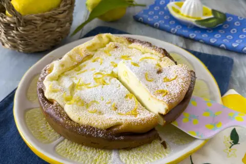Una deliziosa torta ricotta veloce, spolverata di zucchero a velo e scorza di limone, servita su un piatto a forma di limone.