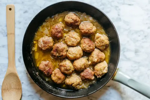 Polpette in bianco cremose in padella, dorate e succulente, pronte per essere gustate con un cucchiaio di legno.