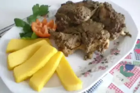 Piatto di coniglio in bianco con polenta e guarnizione di pomodoro e prezzemolo.