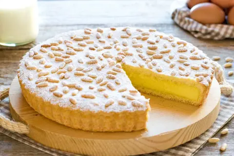 Una deliziosa torta della nonna, con crema gialla e pinoli tostati, spolverata di zucchero a velo.