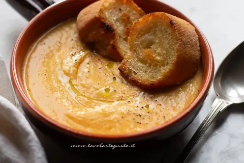 Una ciotola di terracotta con una cremosa zuppa di fagioli, guarnita con crostini dorati e un filo d'olio.