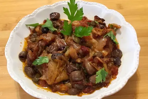 Un piatto invitante di melanzane in agrodolce, con olive nere e capperi, guarnito con prezzemolo fresco.