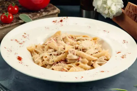 Piatto di pasta del pastore con crema, pollo e formaggio grattugiato, guarnito con paprika.