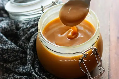 Un cucchiaio raccoglie un filo di caramello salato perfetto, denso e dorato, da un barattolo di vetro.