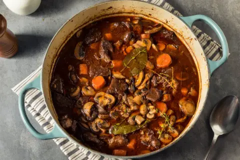 Un invitante spezzatino con funghi, carote e erbe aromatiche in una casseruola blu.