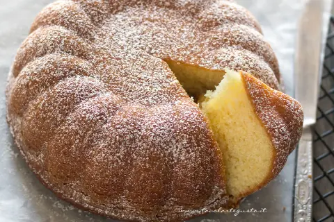 Torta 7 vasetti soffice e dorata, cosparsa di zucchero a velo. Una fetta è stata tagliata, rivelando l'interno profumato.
