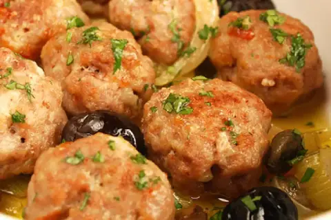 Polpette di carne succulente, dorate e profumate, servite con olive nere e un contorno di verdure.