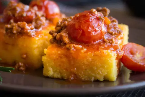 Polenta morbida ricoperta da un ricco sugo con salsiccia e pomodorini. Un piatto confortante e saporito.