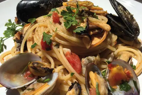 Spaghetti con cozze e vongole, un piatto cremoso e saporito, guarnito con prezzemolo fresco e pomodorini.