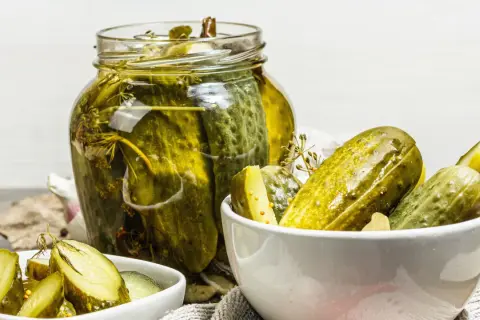 Vaso di cetriolini in agrodolce, con alcuni in una ciotola. Profumo di aneto e spezie.