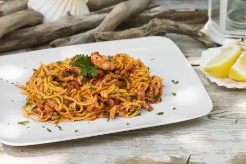 Un piatto di linguine al ragù di pesce, con gamberi e calamari, guarnito con prezzemolo e spicchi di limone su una conchiglia.