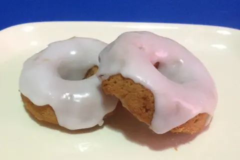 Due ciambelle con glassa per biscotti che si asciuga subito, su un piatto bianco.