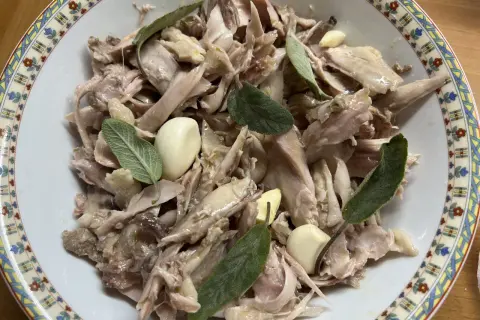 Piatto di tonno di coniglio sfilacciato, condito con aglio e foglie di salvia fresca, servito in una ciotola decorata.
