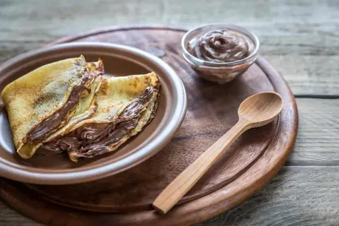 Crepes ripiene di una golosa nutella fatta in casa, pronte per essere gustate con un cucchiaino di legno.