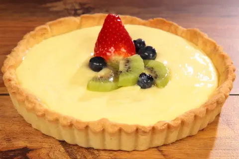 Deliziosa crostata con crema pasticcera, guarnita con fragola, kiwi e mirtilli. Un dolce invitante su un tavolo di legno.