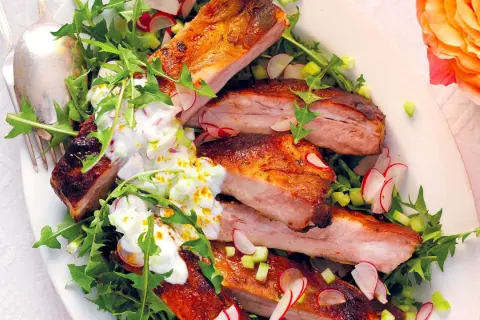 Costine di maiale succulente, perfette per una marinatura saporita, servite su un letto di rucola e ravanelli, con una salsa cremosa.