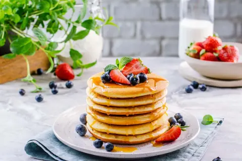 Pila di soffici pancake senza glutine e lattosio, guarniti con fragole, mirtilli e sciroppo d'acero.