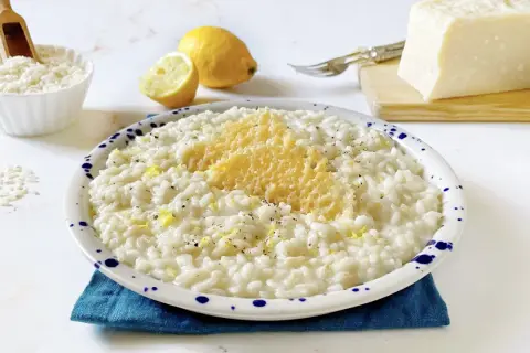Un cremoso riso al limone freddo, guarnito con scorza di limone e parmigiano grattugiato, pronto per essere gustato.